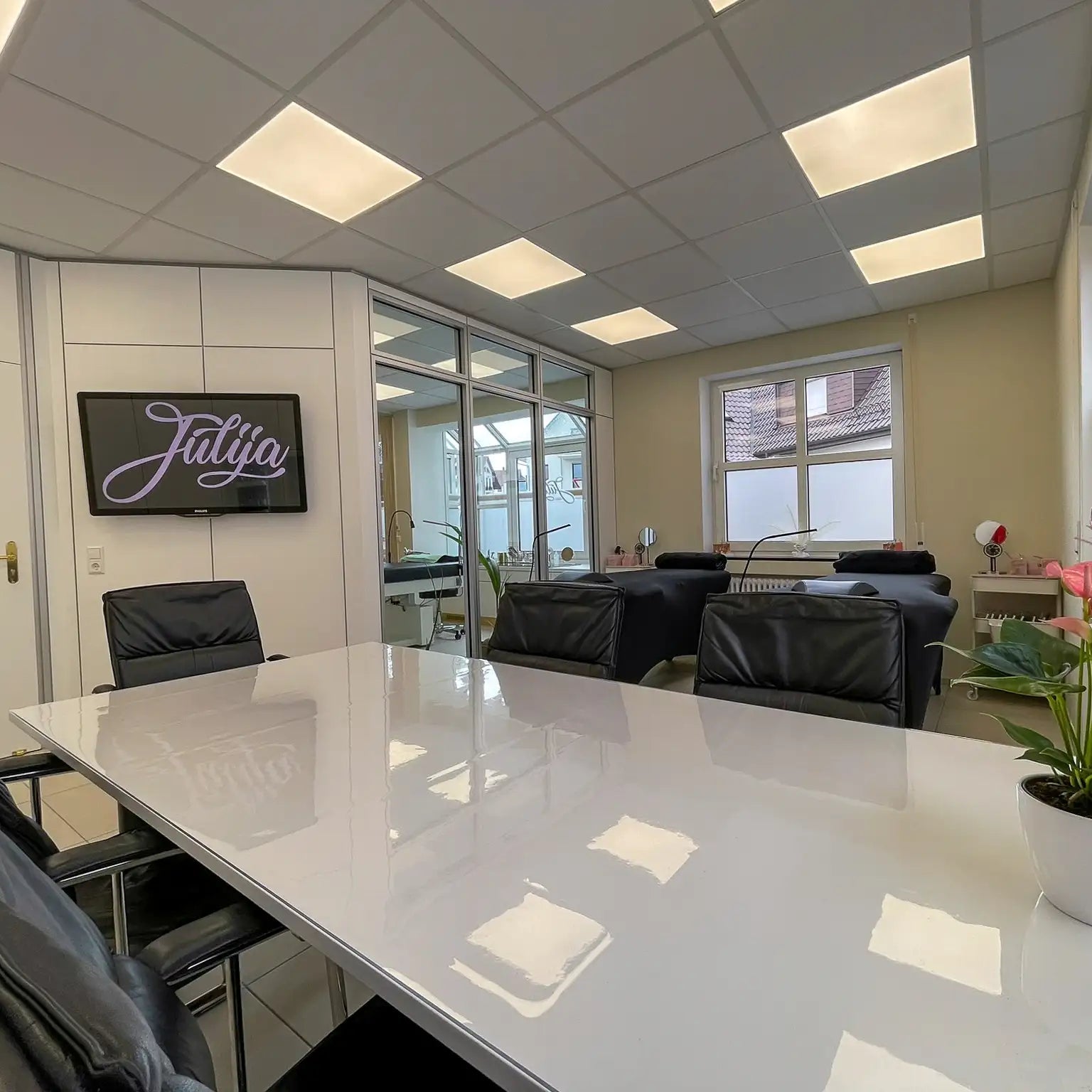 Schulungsraum Wimpernstudio Julija in Stuttgart mit einem Besprechungstisch im Vordergrund und im Hintergrund zwei Behandlungsliegen