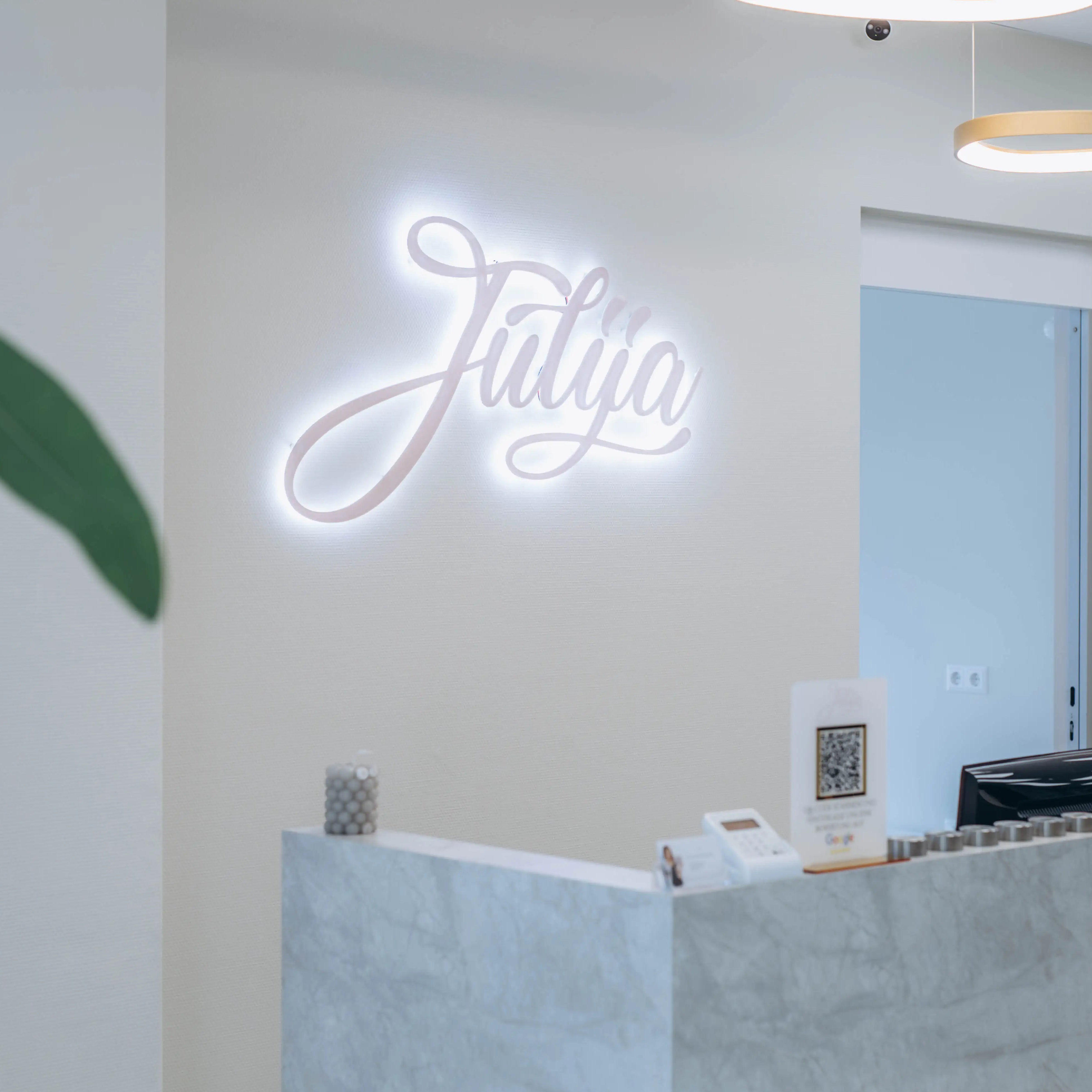 Eingangsbereich Wimpernstudio, im Vordergrund der Empfangs-Theresen in Marmor-Optik, im Hintergrund das Logo Julija mit einer weißen Hintergrundbeleuchtung